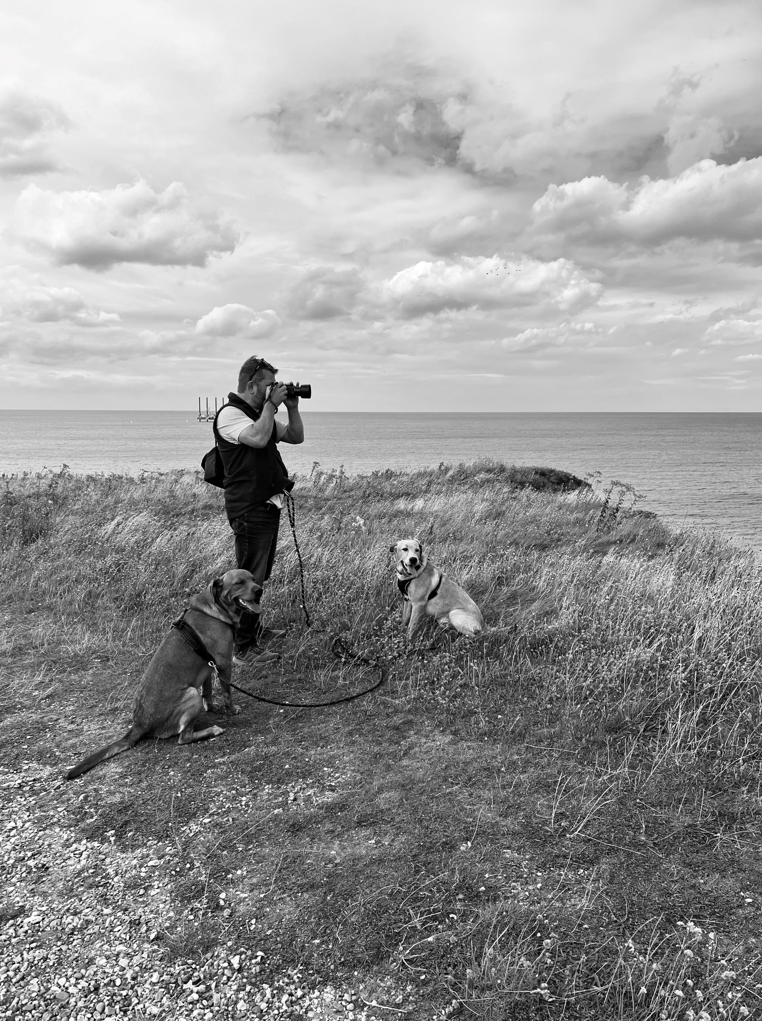 Tom Jolly taking a photo out to sea with his two dogs waiting patiently. Credit to my daughter Jessica Jolly on her iPhone.